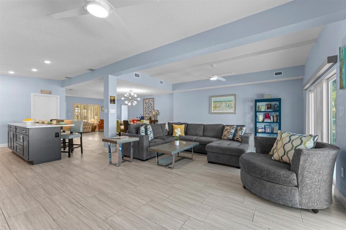 A spacious living room with a grey sofa, a coffee table, and a kitchen area with a grey island and bar stools.