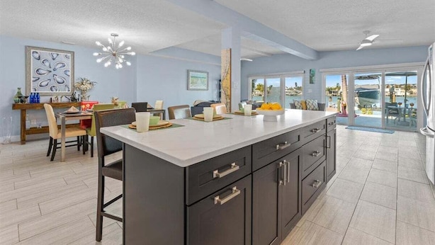 A spacious kitchen with a large island, dark cabinetry, and a dining area with chairs and a table. - Water Lover's Paradise | Waterfront • Private Dock • Heated Pool (Indian Rocks Beach)