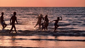 Silhouetten van mensen op het strand tijdens zonsondergang.