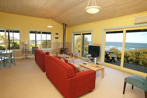 A living room with a red sofa, a television, and a view of the ocean through large windows.