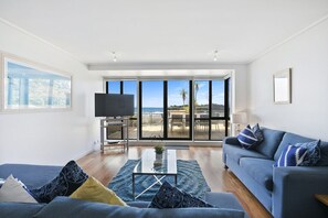 A spacious living room with a large TV, a sofa, and a coffee table. - Apartment 11 Pacific Apartments (Lorne)