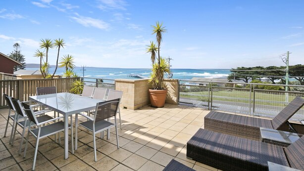 Une terrasse avec une table et des chaises, un pot de fleurs et une vue sur l’océan.
