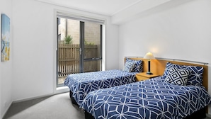 Une chambre avec deux lits, une table de chevet, une lampe et une porte-fenêtre coulissante donnant sur un espace extérieur.