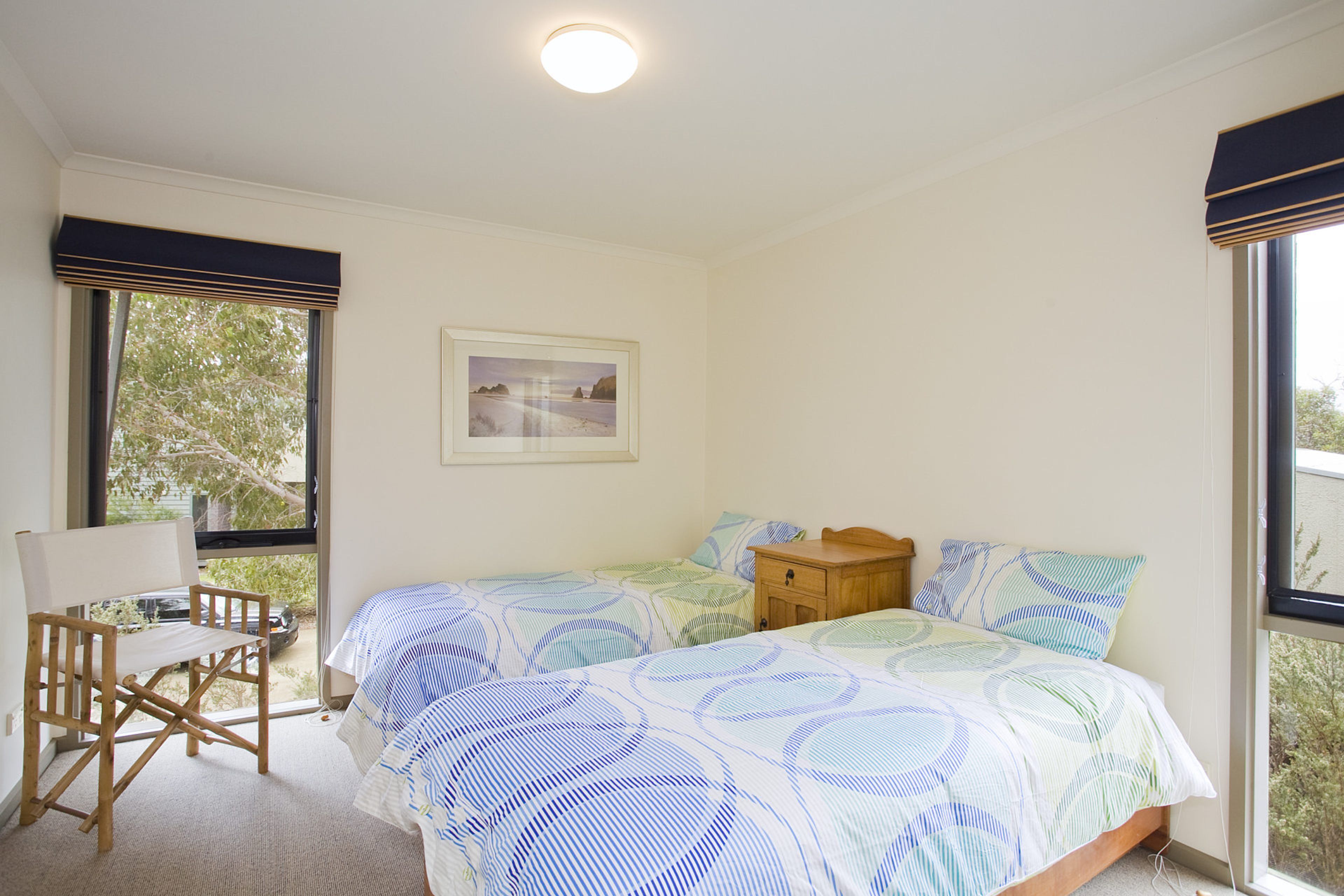 Un dormitorio con cama, una silla, una mesita de noche y un cuadro en la pared.