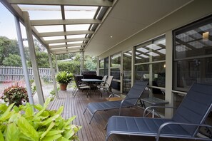 A covered outdoor patio with a table and chairs, a grill, and potted plants.