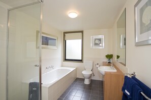 A bathroom with a glass shower enclosure, a bathtub, a toilet, and a sink.