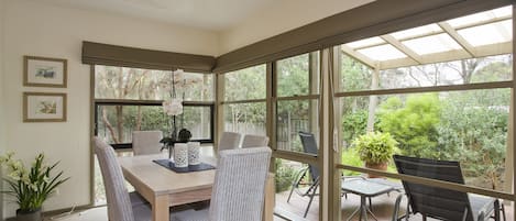 A dining area with a table and chairs, large windows, and a view of greenery outside.