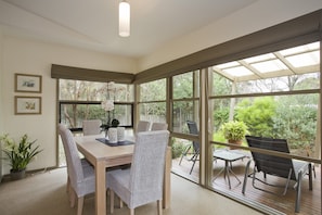 A dining area with a table and chairs, large windows, and a view of greenery outside.
