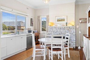 Una cocina moderna con armarios blancos, una mesa de comedor con sillas, una chimenea de piedra y vistas por la ventana.