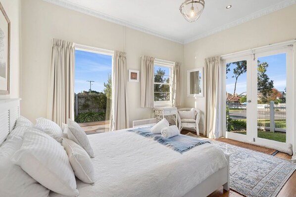 Un dormitorio con una cama grande, un escritorio y una silla, con vistas al exterior a través de las ventanas.