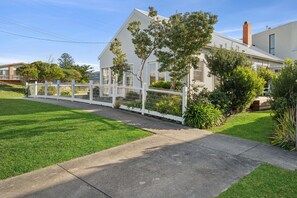Una casa residencial con cerca blanca, césped verde y cielo despejado.