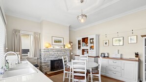 A kitchen with a stone fireplace, white cabinetry, and a dining area with white chairs. - The White House -Prime Location & Oozing Character (Apollo Bay)