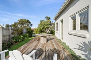 A wooden deck with a concrete table and white chairs, surrounded by a fenced yard with various plants and trees. - The White House -Prime Location & Oozing Character (Apollo Bay)