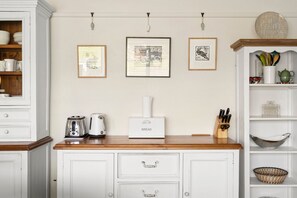 A kitchen with white cabinetry, a toaster, a kettle, and a bread box on the counter. There are three framed pictures on the wall. - The White House -Prime Location & Oozing Character (Apollo Bay)