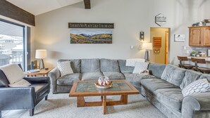A living room with a gray sectional sofa, a wooden coffee table, and a painting of Colorado. - Colorado Escape w/ Pool Access & Mountain Views! (Avon)