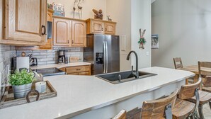 A modern kitchen with wooden cabinets, a stainless steel refrigerator, a large island with a sink, and rustic wooden chairs. - Colorado Escape w/ Pool Access & Mountain Views! (Avon)
