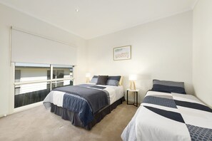A bedroom with two beds, a window with blinds, a bedside table with a lamp, and a framed picture on the wall. - Seaview on Seaview - Exceptional & Spacious With Sensational Views (Apollo Bay)