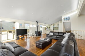 A modern living room with a large black sofa, a wooden coffee table, and a flat-screen TV on a stand. - Seaview on Seaview - Exceptional & Spacious With Sensational Views (Apollo Bay)