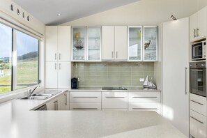 A modern kitchen with white cabinets, a large window, and a view of the outdoors. - Seaview on Seaview - Exceptional & Spacious With Sensational Views (Apollo Bay)