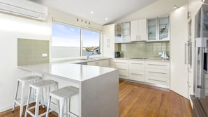 A modern kitchen with a large island, bar stools, a view through the window, and a built-in oven.