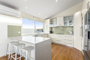 A modern kitchen with a large island, bar stools, a view through the window, and a built-in oven. - Seaview on Seaview - Exceptional & Spacious With Sensational Views (Apollo Bay)