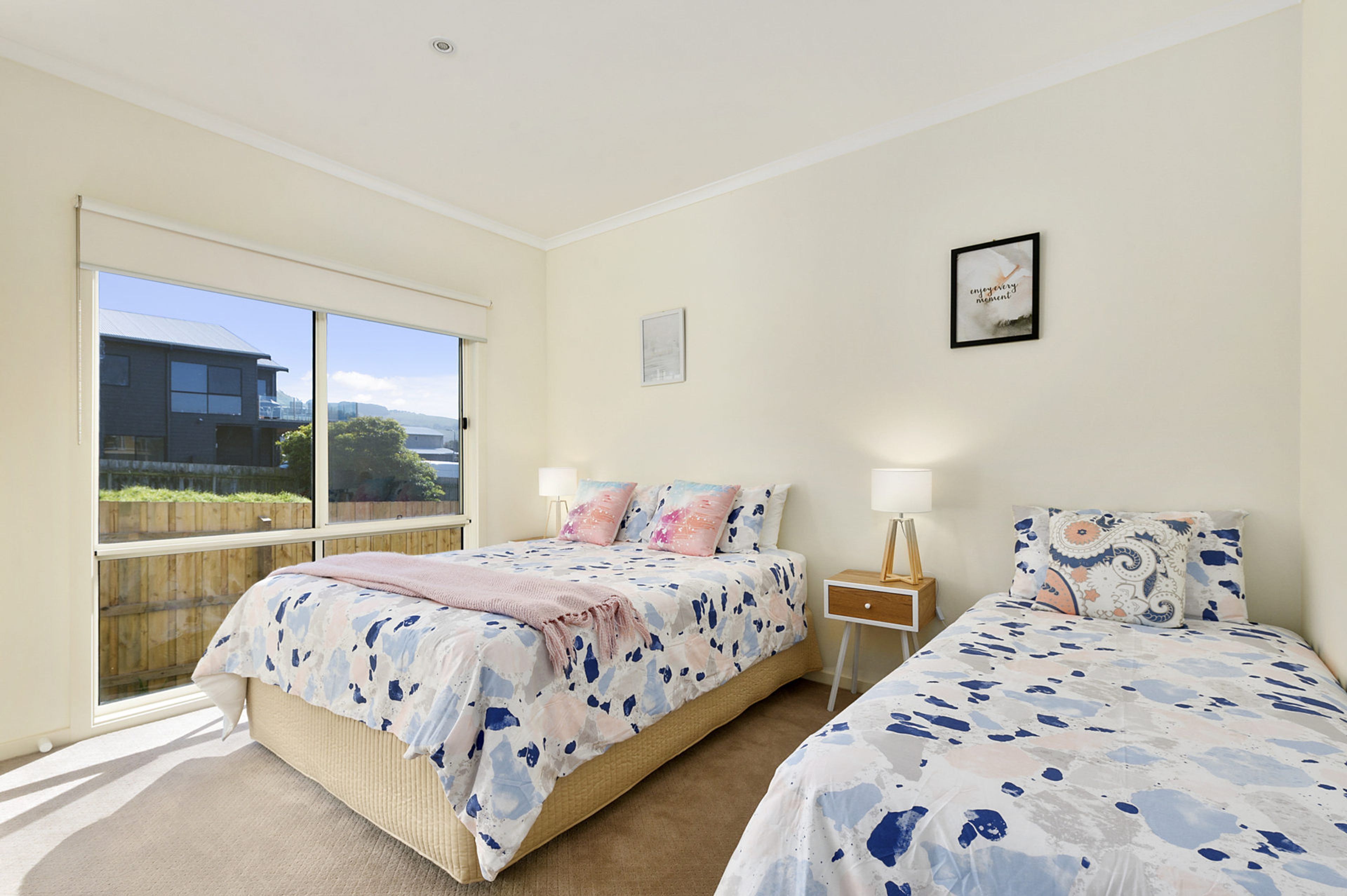 A bedroom with two beds, a window, and a wall-mounted picture.