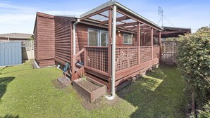 Une maison en bois d’un seul étage, dotée d’une terrasse, d’une cour clôturée et d’un abri de jardin bleu.