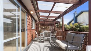 Une terrasse extérieure couverte, dotée d’une plateforme en bois, d’une table avec des chaises et d’un coin salon avec des coussins.