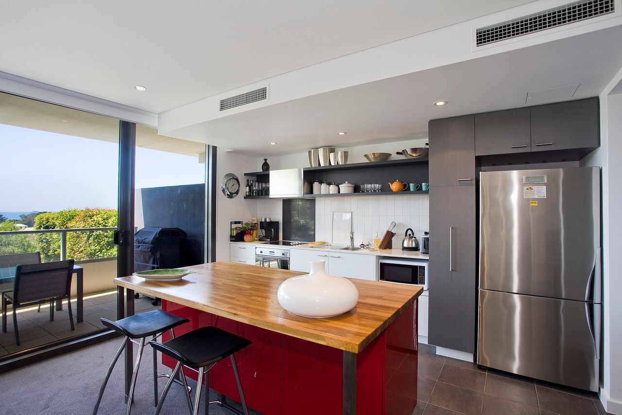 A modern kitchen with a central island, stainless steel appliances, and a view to the outside.