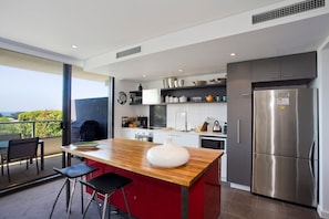 Een moderne keuken met een centraal eiland, roestvrijstalen apparatuur en uitzicht op het buiten.