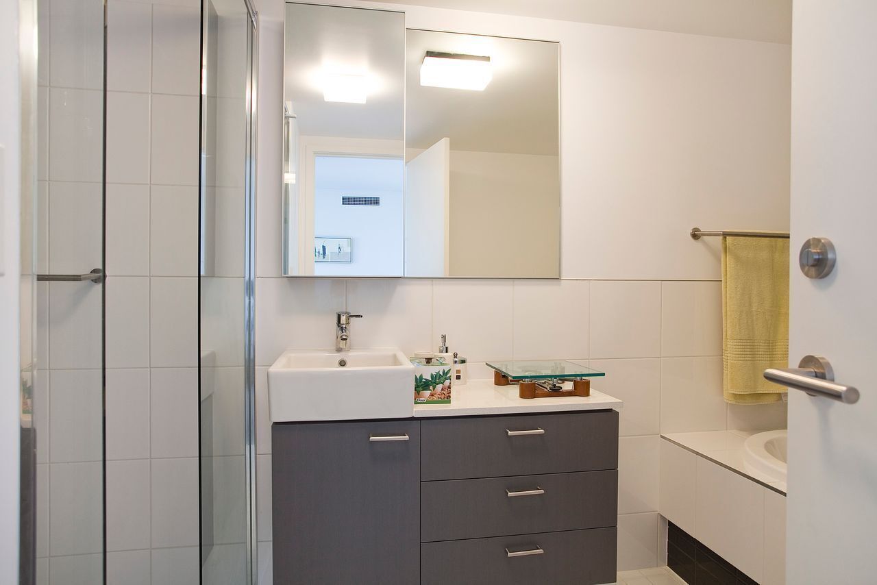 A bathroom with a glass shower enclosure, a white sink, a mirror, and a towel rack.