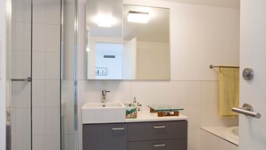 Un baño con cabina de ducha de vidrio, un lavabo blanco, un espejo y un perchero para toallas.