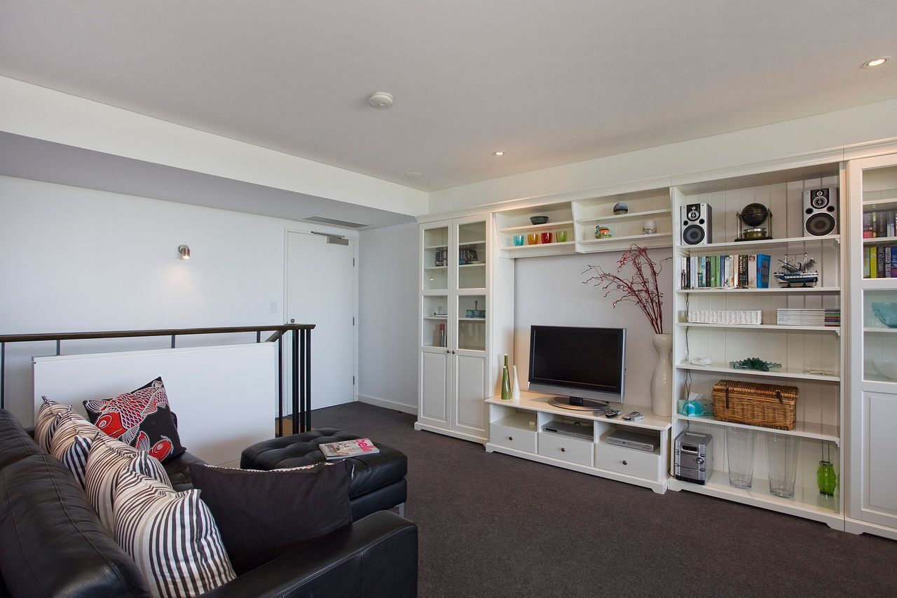 A modern living room with a black leather sofa, a flat-screen TV, and a white entertainment unit with shelves.