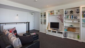 Una sala de estar moderna con un sofá de cuero negro, un televisor de pantalla plana y un mueble blanco para televisión con estantes.
