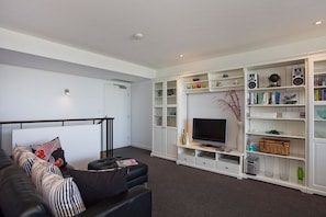 Een moderne woonkamer met een zwarte leren bank, een flatscreentelevisie en een witte tv-meubel met planken.