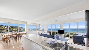 A modern kitchen with a large island, a dining area with a view, and a living space with a sofa and TV.