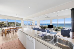 Een moderne keuken met een groot eiland, een eethoek met uitzicht en een zithoek met een bank en televisie.