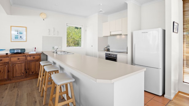 A modern kitchen with a central island, wooden stools, white cabinetry, and a built-in oven.