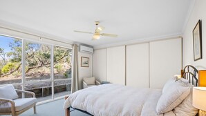 A bedroom with a large bed, a chair, a desk, and a window with a view of trees. - Beach View (Fairhaven)