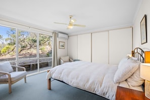 A bedroom with a large bed, a chair, a desk, and a window with a view of trees. - Beach View (Fairhaven)