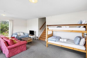 A room with a bunk bed, a sofa, a television, and a staircase.