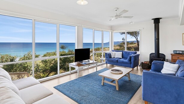 A spacious living room with a large window overlooking the sea, a blue sofa, a white armchair, and a wooden coffee table. - Beach View (Fairhaven)