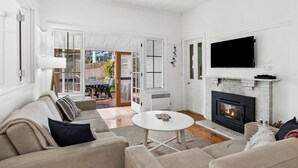 A living room with a fireplace, a television mounted above it, and a sofa with cushions. - Sur La Mer (Lorne)