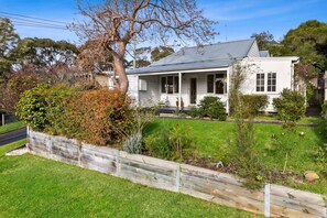 A single-story house with a front porch, surrounded by a well-maintained lawn and a wooden fence.