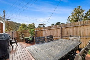 A wooden deck with a table and chairs, surrounded by a wooden fence, and a barbecue grill. - Sur La Mer (Lorne)