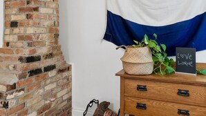 A room with a brick fireplace, wooden dresser, and a wall with a blue and white striped fabric. - Sur La Mer (Lorne)
