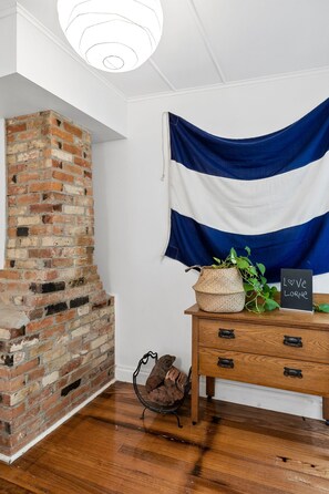 Ein Zimmer mit einem Kamin aus Ziegelsteinen, einem Holzschrank und einer Wand mit blau-weiß gestreifter Stofftapete.
