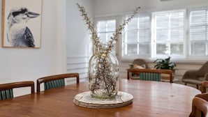 A dining table with a glass vase containing dried plants, surrounded by chairs. - Sur La Mer (Lorne)