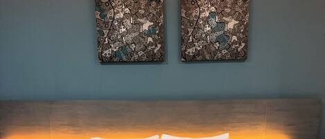 A hotel room with a large bed, two nightstands, a headboard with a light, and two abstract paintings on the wall.