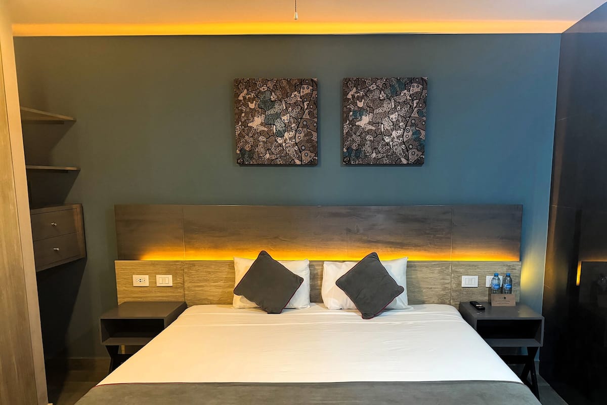 A hotel room with a large bed, two nightstands, a wooden headboard, and two wall-mounted artworks.